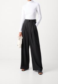 Valkoinen poolopaita, mustat leveälahkeiset housut, joissa on laskokset, ja pieni valkoinen käsilaukku. Jalkineina mustat avoimet liukusandaalit.