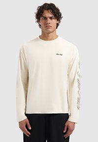 Long-sleeve cream t-shirt made of soft fabric. Features a small "Pure Talks" logo on the chest and a text design along the right sleeve.