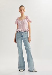 Paita vaaleanpunaisista, puff-hihoista, jossa on röyhelöreunat, nappiyksityiskohtia ja muotoiltu yläosa, yhdistettynä vaaleansinisiin levenevähihoisiin farkkuihin ja valkoisiin kenkiin.