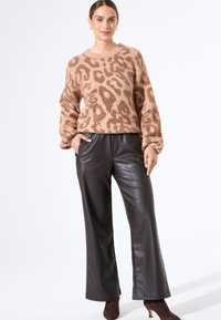 Beige Leopard-Print-Pullover mit einer flauschigen Textur, kombiniert mit dunkelbraunen, weiten Lederhosen, getragen mit braunen, hohen Stiefeln.