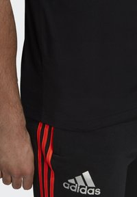 Mustapaitainen urheilu paita lyhyillä hihoilla, yhdistettynä mustiin pantsuihin, joissa on punaiset sivusuunnat ja hopeinen Adidas-logo vyötärön lähellä.