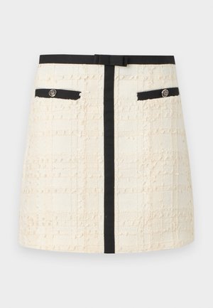 Krémově texturovaná mini sukně s černým pasem, svislým pruhem, předními kapsami s černým lemováním a dekoračními knoflíky.