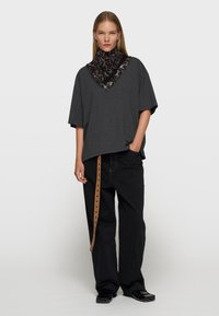 Camiseta gris de gran tamaño combinada con pantalones negros de pierna ancha que cuentan con un cinturón marrón con agujeros. Se lleva una bufanda de estampado de leopardo alrededor del cuello.