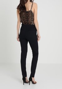 Black fitted pants with a smooth texture, paired with a leopard print camisole. Open back design and thin straps. Closed-toe high heels.