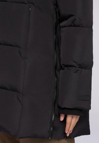 Schwarze Steppjacke mit einem gesteppten Design, ausgestattet mit einem Reißverschluss, elastischen Bündchen und einer versteckten Reißverschlusstasche an der Seite.