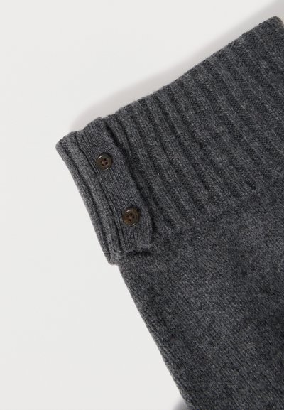 Tissu tricoté côtelé gris foncé avec deux boutons marron sur le bord du poignet plié sur fond blanc.