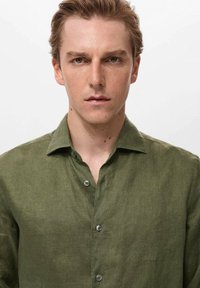 Olive green linen shirt with a button-up front, collar, and long sleeves. Features a textured fabric and contrasting buttons.