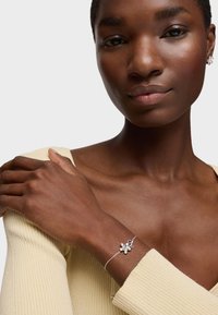 Bracciale d'argento con design floreale e dettagli in gemme, indossato su un polso snello, abbinato a un top a maniche lunghe a coste leggero.