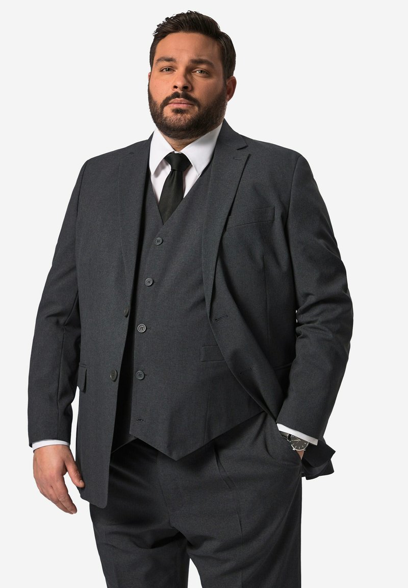 Completo tre pezzi grigio scuro con rever a toppa, giacca monopetto e gilet abbinato. Presenta una camicia bianca e una cravatta nera.
