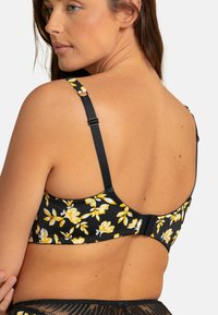 Soutien-gorge noir à motifs floraux avec des accents jaunes, doté de bretelles réglables et d'une fermeture à crochets au dos. Texture de tissu lisse.