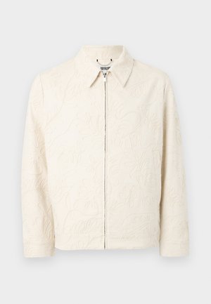 Beige výšivková bunda s límečkem, zipovým zapínáním a texturovanými květinovými vzory. Vyrobená z hladkého materiálu, má dlouhé rukávy a přiléhavý střih.
