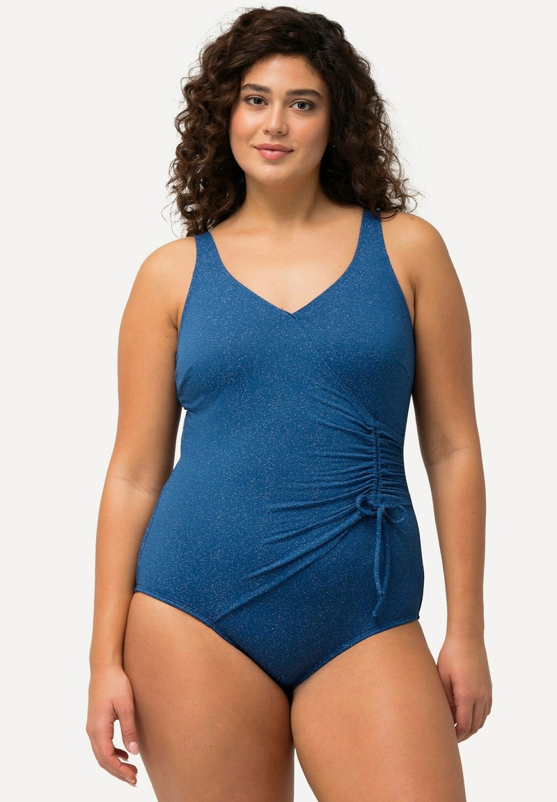 Maillot de bain une pièce bleu marine avec un subtil éclat. Il présente un décolleté en V, un ruché sur les côtés ajustable et un détail à nouer. Tissu doux et design sculptant.