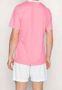 Rosa idrottströja med korta ärmar, rund hals, slät textur och vita accenter; matchad med vita shorts.