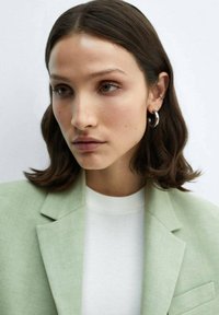 Light green linen blazer over a white sweater. The subject has shoulder-length dark hair and wears silver hoop earrings.