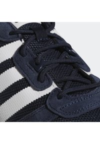 Marinblå träningsskor i mesh och mocka, med svarta snören, tre vita ränder och strukturerad detaljering på ovandelen.