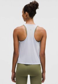 Top deportivo blanco sin mangas con diseño de espalda nadadora, hecho de tela ligera, combinado con leggings de talle alto en verde oliva.