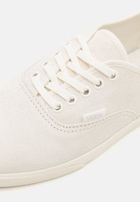 White suede sneaker featuring a low profile, round toe, six eyelet lace-up design, and a small logo patch on the side.