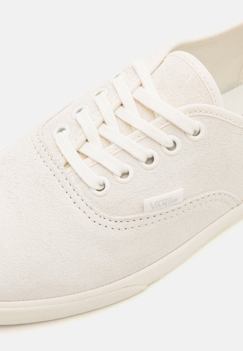 Zapatilla de ante blanca con diseño de perfil bajo, punta redonda, cierre de seis ojales con cordones y un pequeño parche con el logo en el lateral.