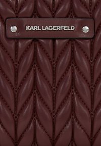 Bordo kvadrirani kožni ranac s pletenim uzorkom, s metalnom oznakom srebrne boje koja glasi "KARL LAGERFELD" i sjajnim metalnim detaljima.