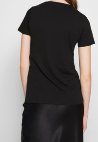 Camiseta de algodón negra con cuello redondo clásico y mangas cortas, con una textura suave y un diseño sencillo, llevada con una falda negra.