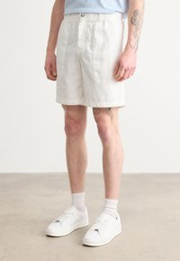Linen shorts vaaleassa bežissä, joissa on kaksi etutaskua ja rento istuvuus. Yhdistettyinä valkoisiin tennareihin ja nilkkasukkiin.