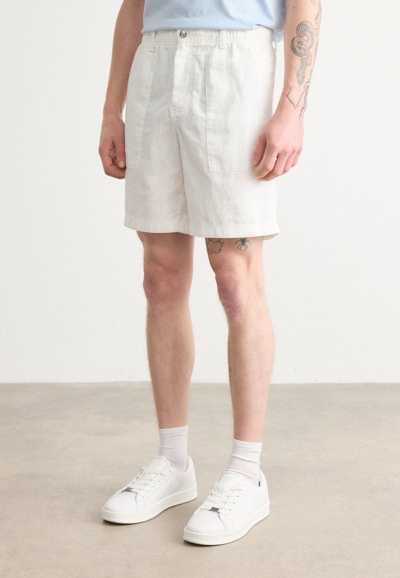 Linen shorts vaaleassa bežissä, joissa on kaksi etutaskua ja rento istuvuus. Yhdistettyinä valkoisiin tennareihin ja nilkkasukkiin.