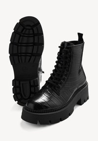Botte à plateforme noire épaisse avec lacets, texture crocodile et semelle épaisse rainurée, vue de côté et de dessous.