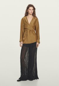 Top marrone avvolgente con maniche lunghe e design attorcigliato, abbinato a pantaloni larghi plissettati neri con una finitura testurizzata.