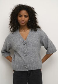 Pilkas megztas kardiganas su V formos iškirpte, trumpomis rankovėmis ir trimis dekoratyviniais gėlės formos mygtukais priekyje. Faktūrinis ribotas kraštas.