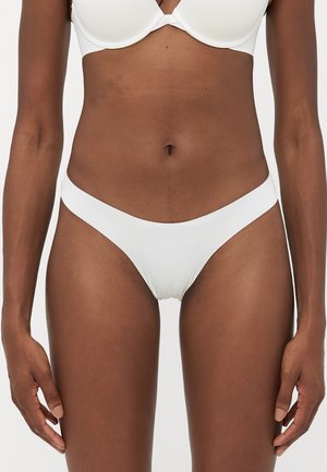 Woman wearing white seamless underwear and bra, showing midsection and upper thighs against a plain background.