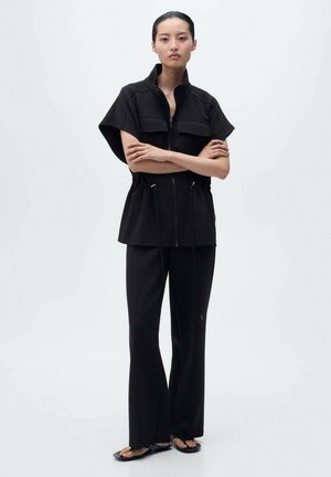 Schwarzes Zip-Up-Top mit kurzen Ärmeln und zwei vorderen Taschen, kombiniert mit lockeren schwarzen Hosen. Glattes Material mit minimalistischem Design.
