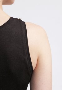 Zwart mouwloos topje met een ribbelstructuur, voorzien van decoratieve hardware accenten op de schouder, vanuit de achterkant gezien.