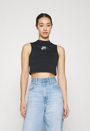 Top corto nero a costine con scollo alto e logo Nike bianco. Abbinato a jeans azzurri a vita alta, creando un look casual e aderente.
