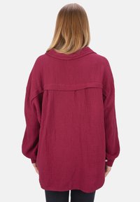 Bordeauxrotes Oversize-Hemd aus strukturiertem, zerknittertem Stoff. Verfügt über lange Ärmel, einen Kragen und einen Knopf-Details an den Manschetten.