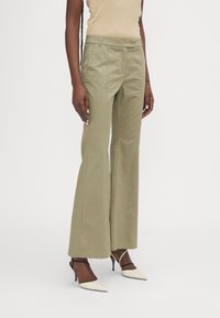 Pantalons évasés verts olive avec un devant plat, fabriqués en tissu mélangé de coton, dotés de poches latérales et d'une coupe ajustée.