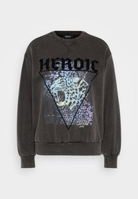 Tummanharmaa huppari, jossa on leopardigrafiikka kolmion muotoisessa kehykseessä, ja sanan "HEROIC" paksuilla mustilla kirjaimilla yläpuolella.