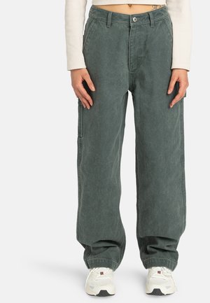 Green cotton cargo pants with a loose fit, featuring side pockets and a high waist, paired with light-colored sneakers.