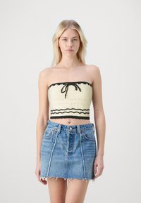 Häkelstil, cremfarbenes Bandeau-Top mit schwarzen Akzenten und vorn gebunden, kombiniert mit einem blauen Denim-Minirock mit ausgefranstem Saum und vorderen Nähten.