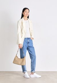 Hvid dobbeltbrystet blazer, ribbet cremet sweater, blå høj talje denim jeans, hvide sneakers med pink detaljer og en beige håndtaske.