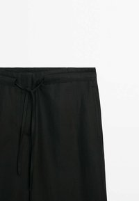 Pantalon décontracté noir avec taille à cordon et poches latérales, présenté sur fond blanc.