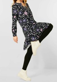 Svart blommig klänning med långa ärmar, prydd med rosa och blå blommor, bärs över svarta leggings, i kombination med vita hög-över-känger.