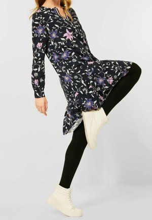 Schwarzes Blumenkleid mit langen Ärmeln, verziert mit rosa und blauen Blumen, getragen über schwarzen Leggings, kombiniert mit weißen High-Top Sneakers.