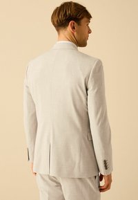 Veste de costume gris clair en tissu texturé, dotée d'un fente simple à l'arrière, de revers crantés et de manches à bouton.