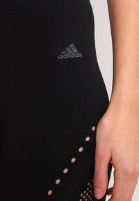Czarne legginsy sportowe o miękkiej teksturze. Posiadają delikatne logo Adidas, a także siateczkowe detale z małymi wycięciami wzdłuż dolnej krawędzi.