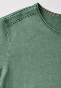 Pull en maille verte avec un col rond. Présente un tissu texturé et des coutures ton sur ton. Rehaussé d'une subtile ligne rouge au niveau du col.