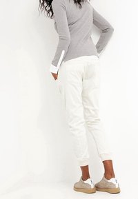 Joggers de algodón blancos con puños elásticos, con bolsillos laterales. Combinados con una camiseta de manga larga gris y zapatillas beige con suelas blancas.