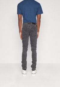 Mörkgrå slim fit-jeans med slitna detaljer, kontrasterande sömmar och bakfickor. Bärs med en blå t-shirt och vita sneakers.