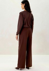 Brown long-sleeve top with puffed shoulders, paired with high-waisted, wide-leg brown trousers. Smooth texture, minimal detailing, and classic fit.