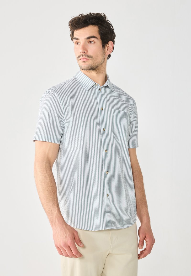 Chemise à manches courtes à rayures verticales bleues et blanches, avec un col, une patte de boutonnage et une poche poitrine. Tissu léger, coupe décontractée.