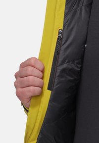 Gelbe Außenjacke mit schwarzem, isoliertem Innenfutter, ausgestattet mit einer Reißverschlusstasche auf der Innenseite und kontrastierenden Nähdetails.